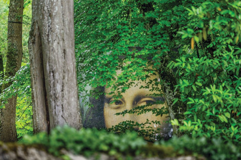 A large mural of the Mona Lisa peers through the trees in the In the Leonardo da Vinci Park in the Loire Valley