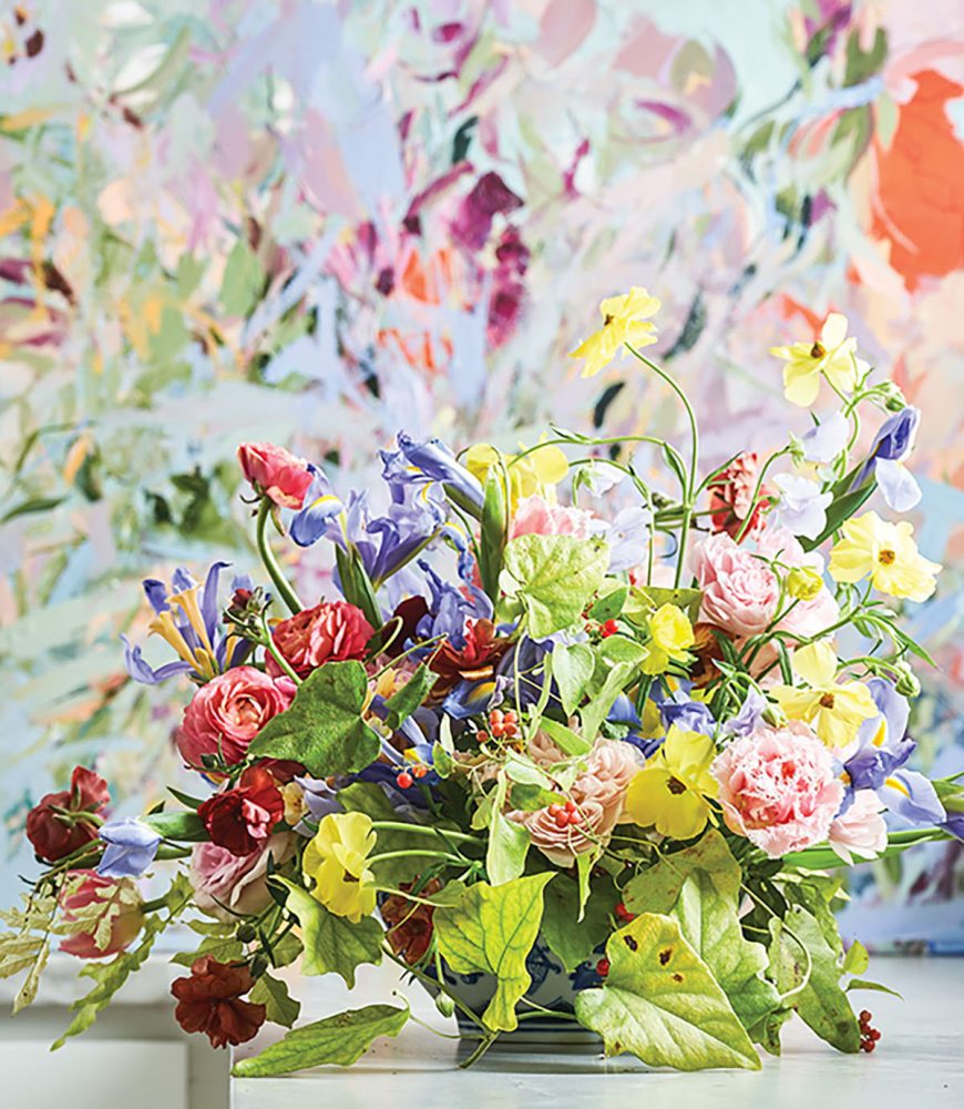 A garden arrangement in a rainbow of colors in front of a Marcy Cook floral painting of the same palette 