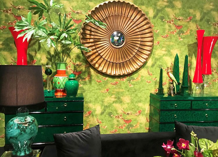 A scene from Maison&Objet features a deep green , lacquered chest of drawers against a tropical-inspired wallpaper