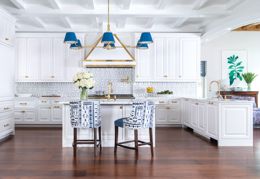 A bright white kitchen is accented with deep blue lampshades and blue patterned chairs.