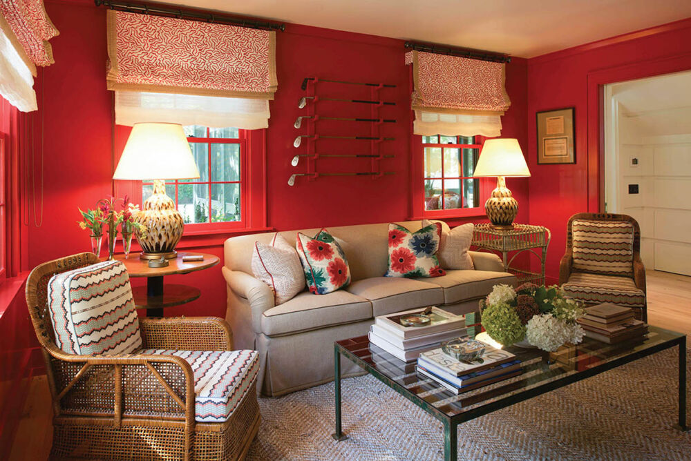 Den with walls painted a bold red. Collection of golf clubs on wall above sofa. Arrangement of hydrangeas on coffee table.