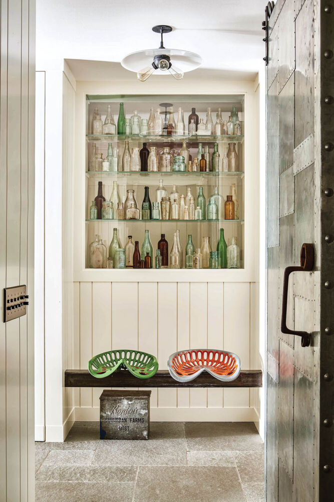 Farmhouse mudroom with whimsical tractor seats and shelves filled with a vintage bottle collection.