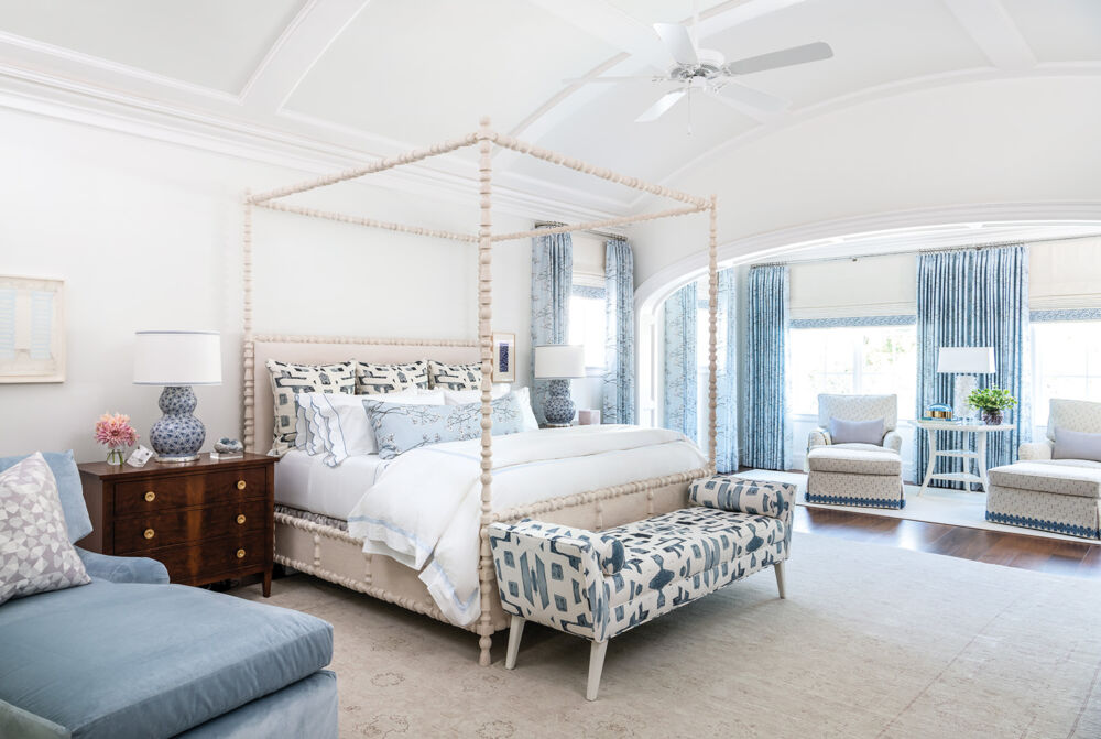 A few pieces of light blue patterned furnishing fill a white bedroom with a tall vaulted ceiling.