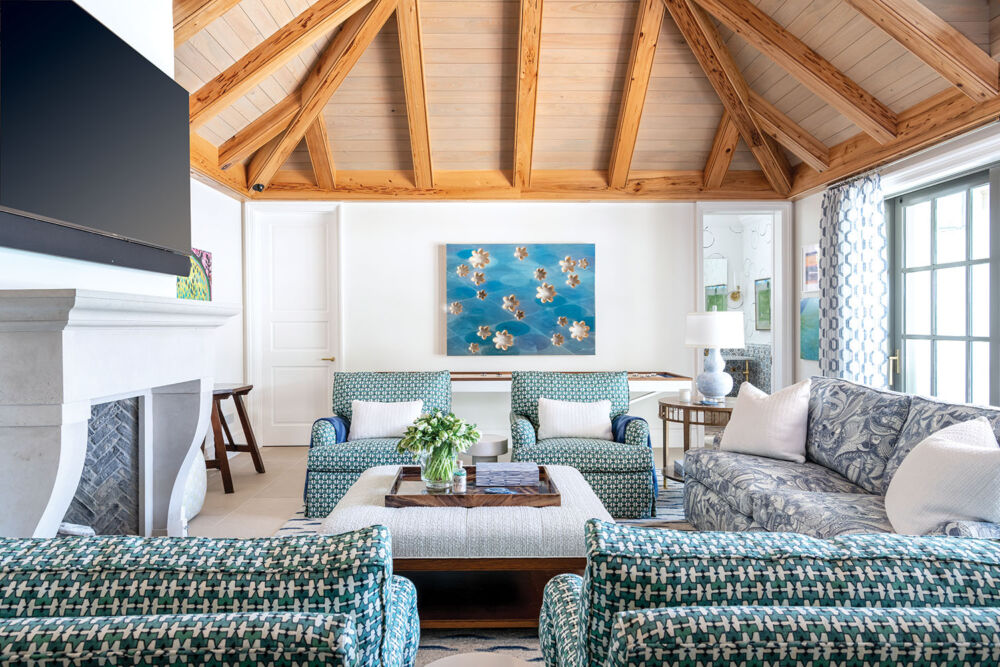 Teal patterned furniture fill a white pool house with a wood vaulted ceiling.
