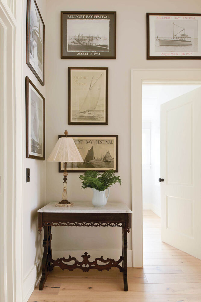 Hallway with white walls and door trim. Vintage images of boats hang over an antique table and the doorway.
