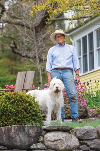 Bruce Lockhart stands in front of his yellow house with his white dog at Swift River farm.