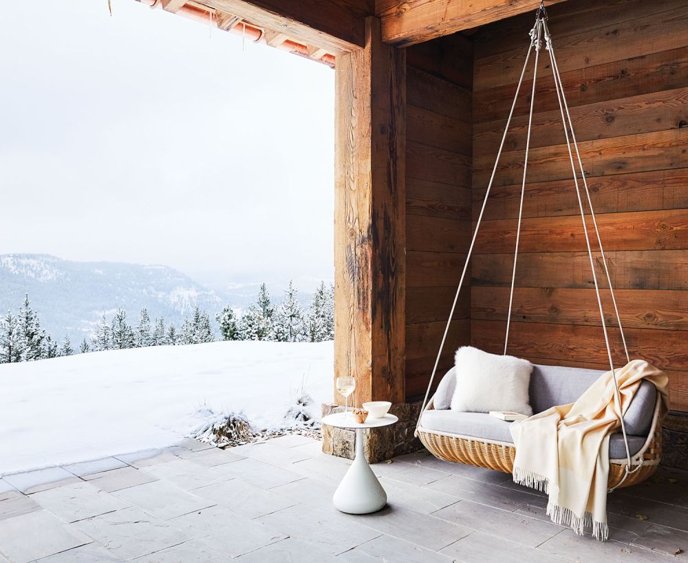 A cozy hanging seat on the deck looking over a snow covered mountain.