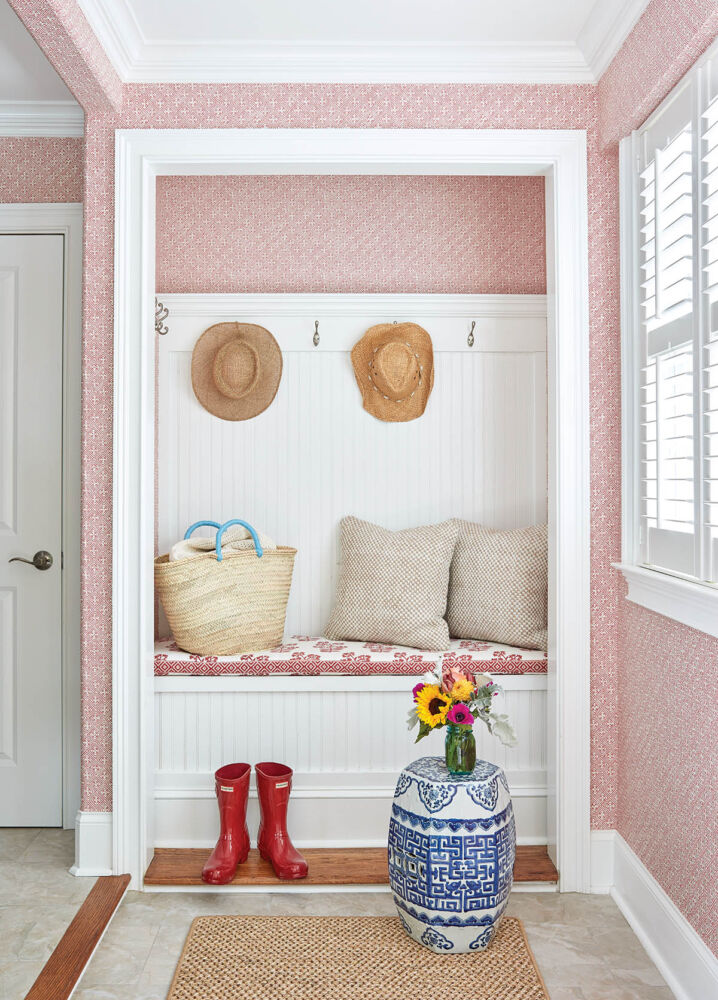 Mudroom with built-in bench in nook and red and white Thibaut wallpaper on walls.