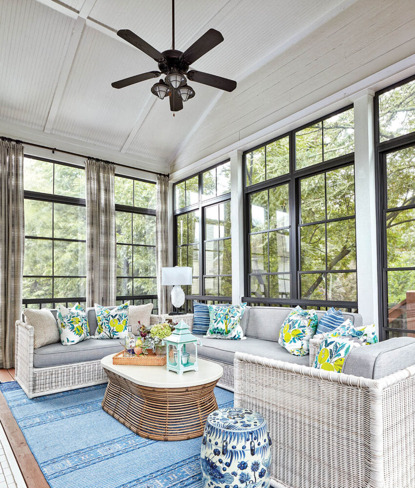 Screened porch with white wicker furniture, colored pillows and garden stools on a blue and white rug.