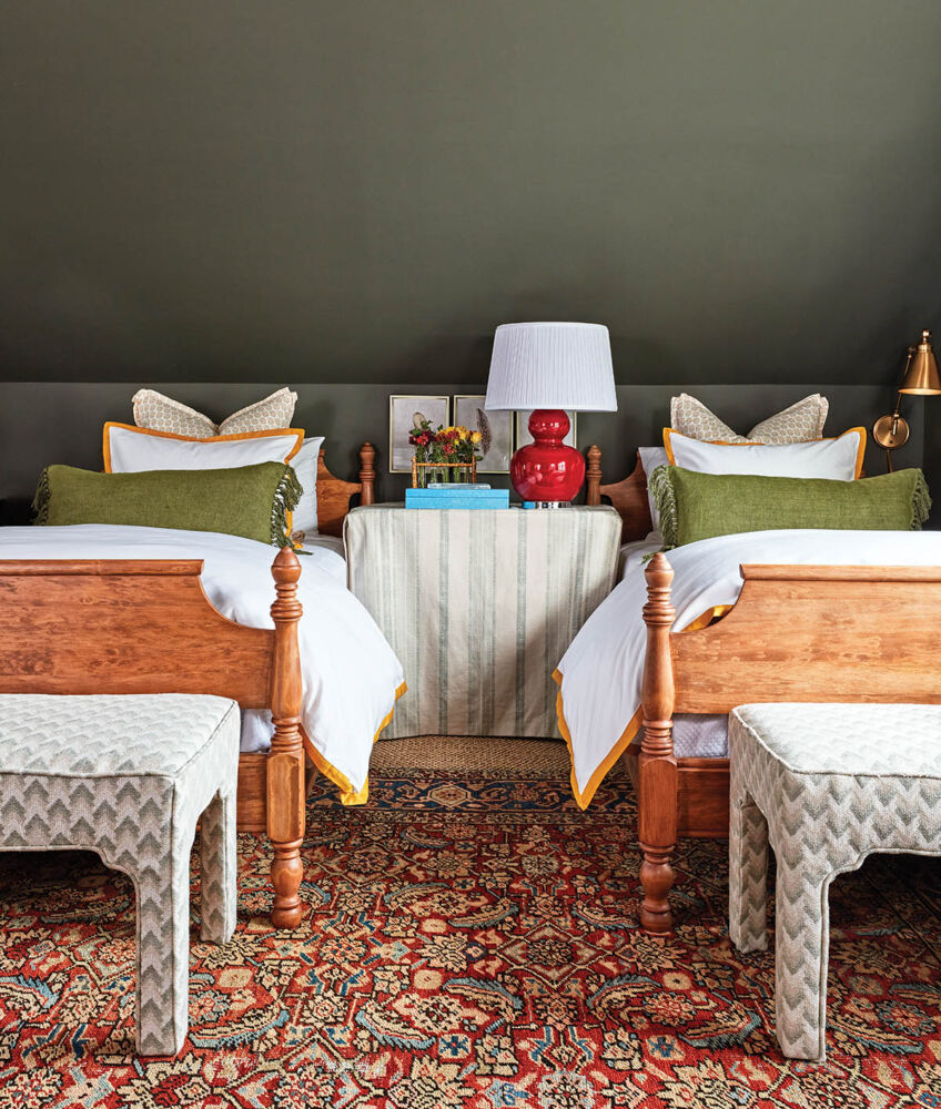 Twin beds in a guest bedroom with dark olive painted walls and sloping ceiling in a Maggie Griffin designed cottage.