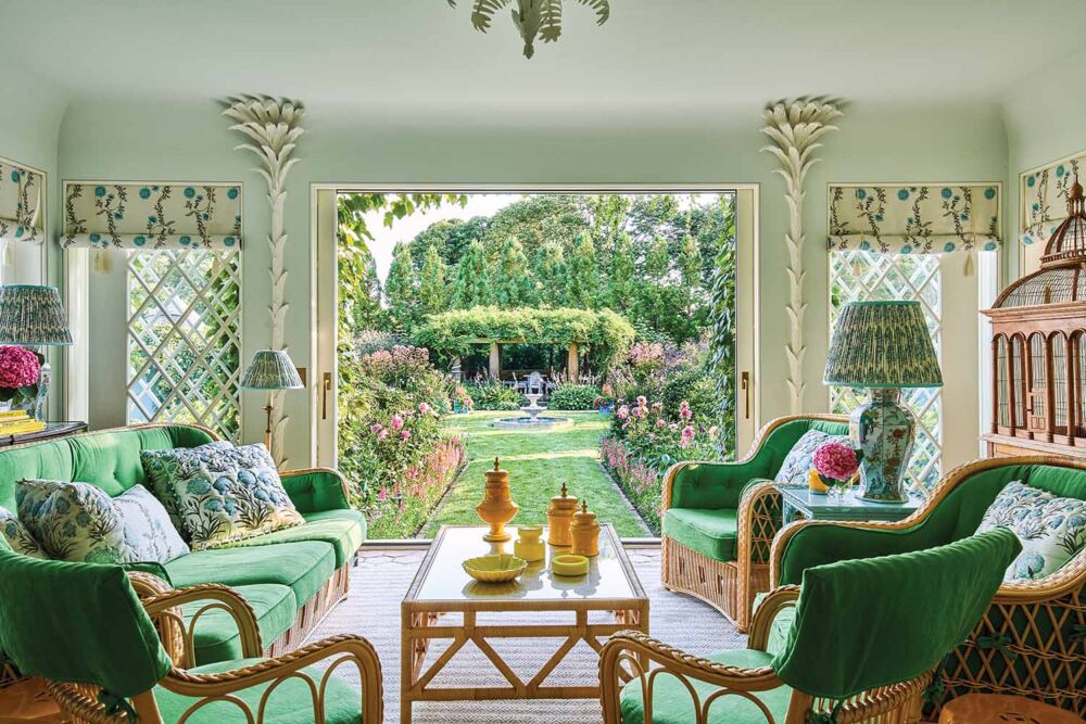 Bright viridian green furniture fills an old fashioned sun room that opens to a bountiful flower garden.