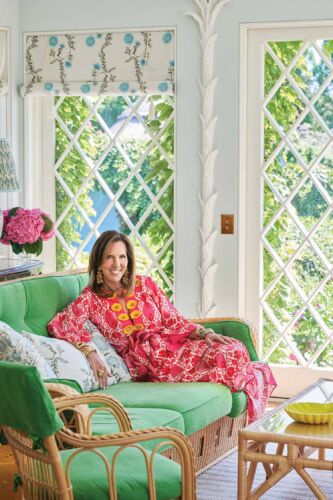 Liz Lange lounges on a viridian green wicker love seat in a bright coral summer dress.