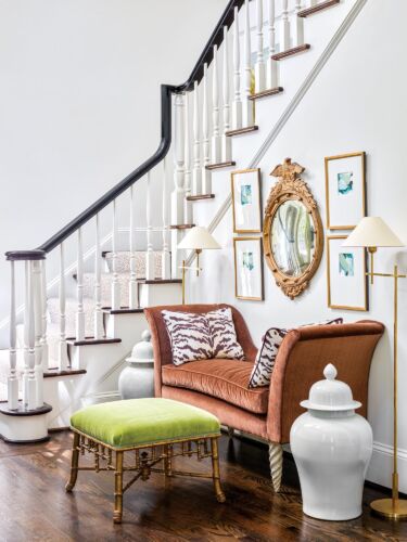 A brown velvet settee sits in a white foyer with stairs behind it.