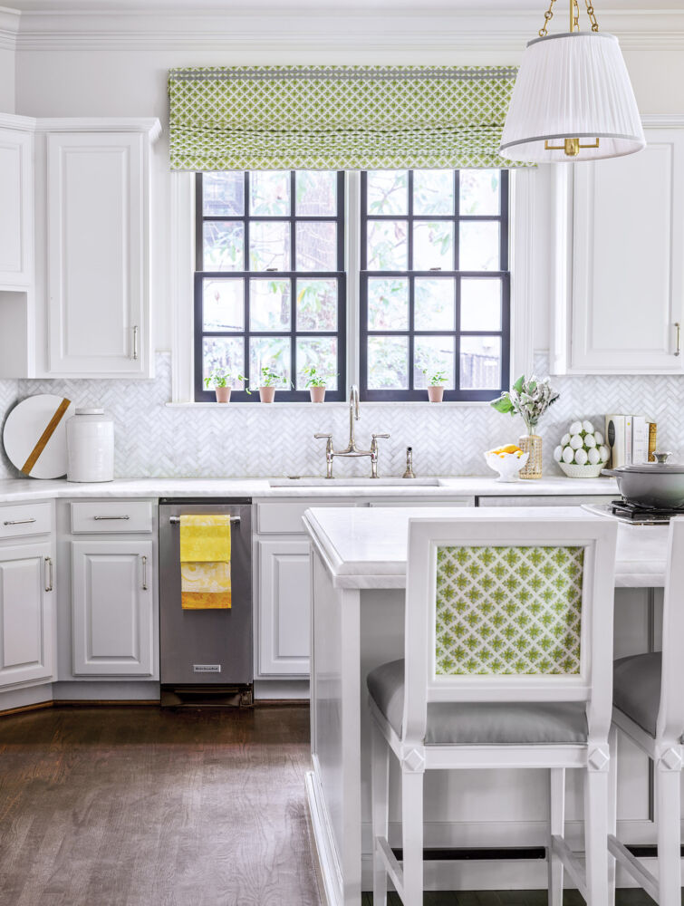 A green cane pattern covers the back of a kitchen island stool inside a bright white kitchen.