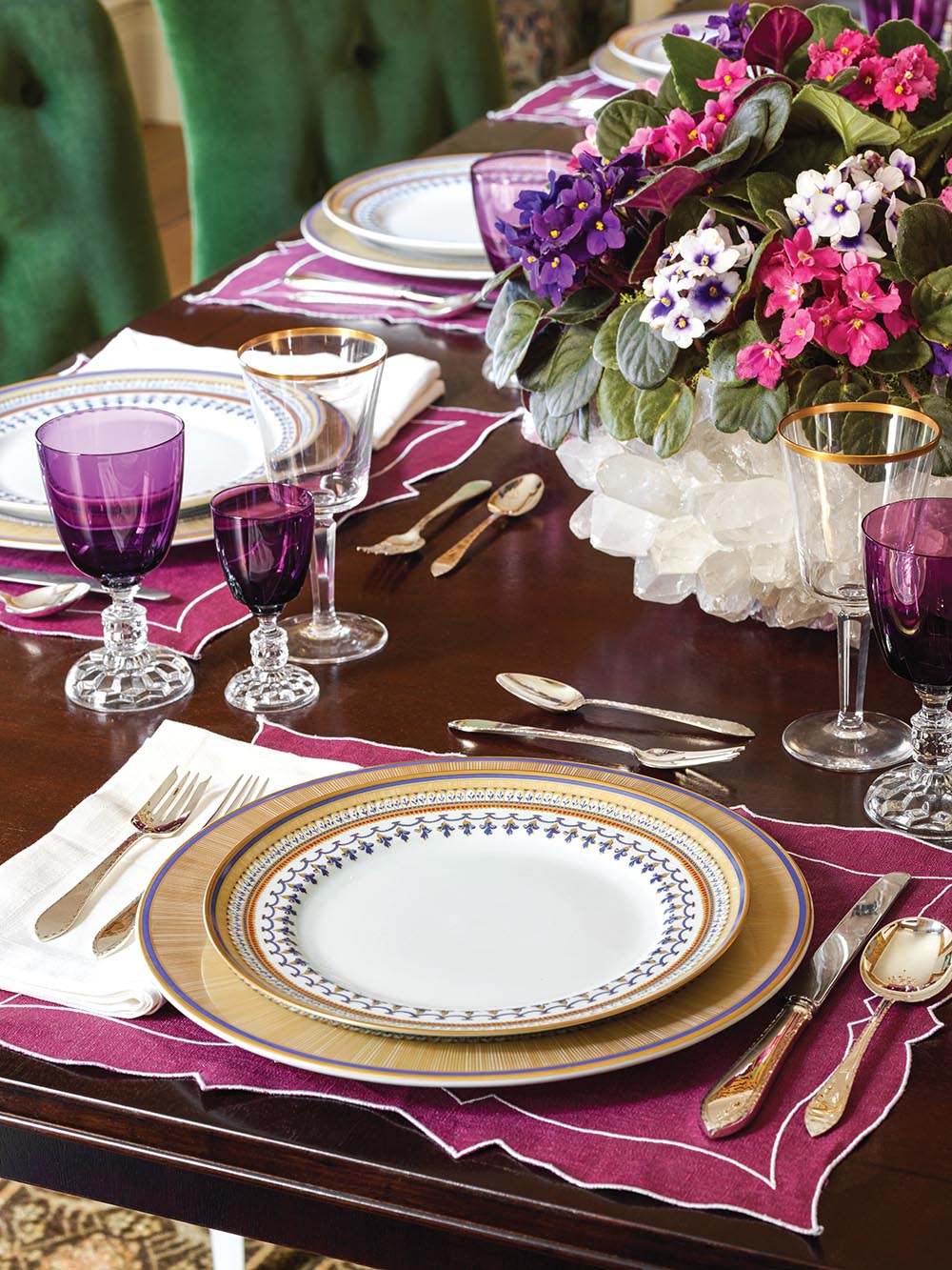 Gold-rimmed china and purple glassware on mahogany table.