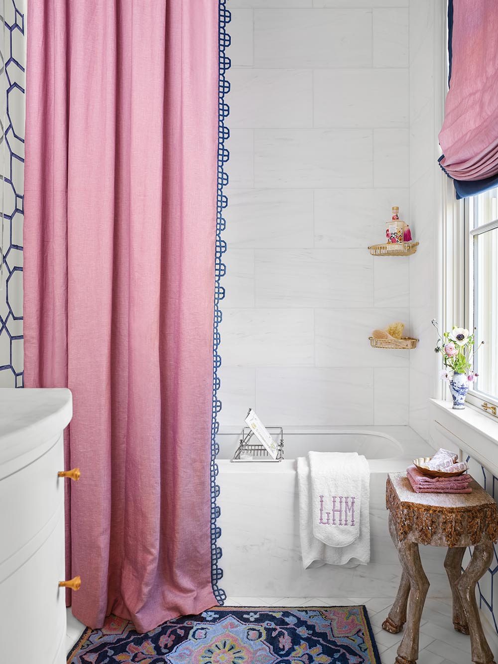 En suite bathroom designed by Lisa Mende with pink shower curtain and window covering. The trim on the leading edge of the curtains references back to the wallpaper pattern in the bath and on the bedroom ceiling.