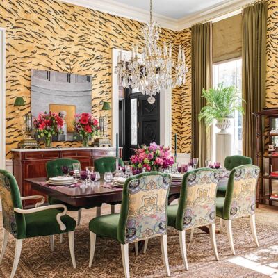 Dining room with hand-painted tiger wallpaper designed by Alexa Hampton, white-wood chairs upholstered in green and pink flowers.