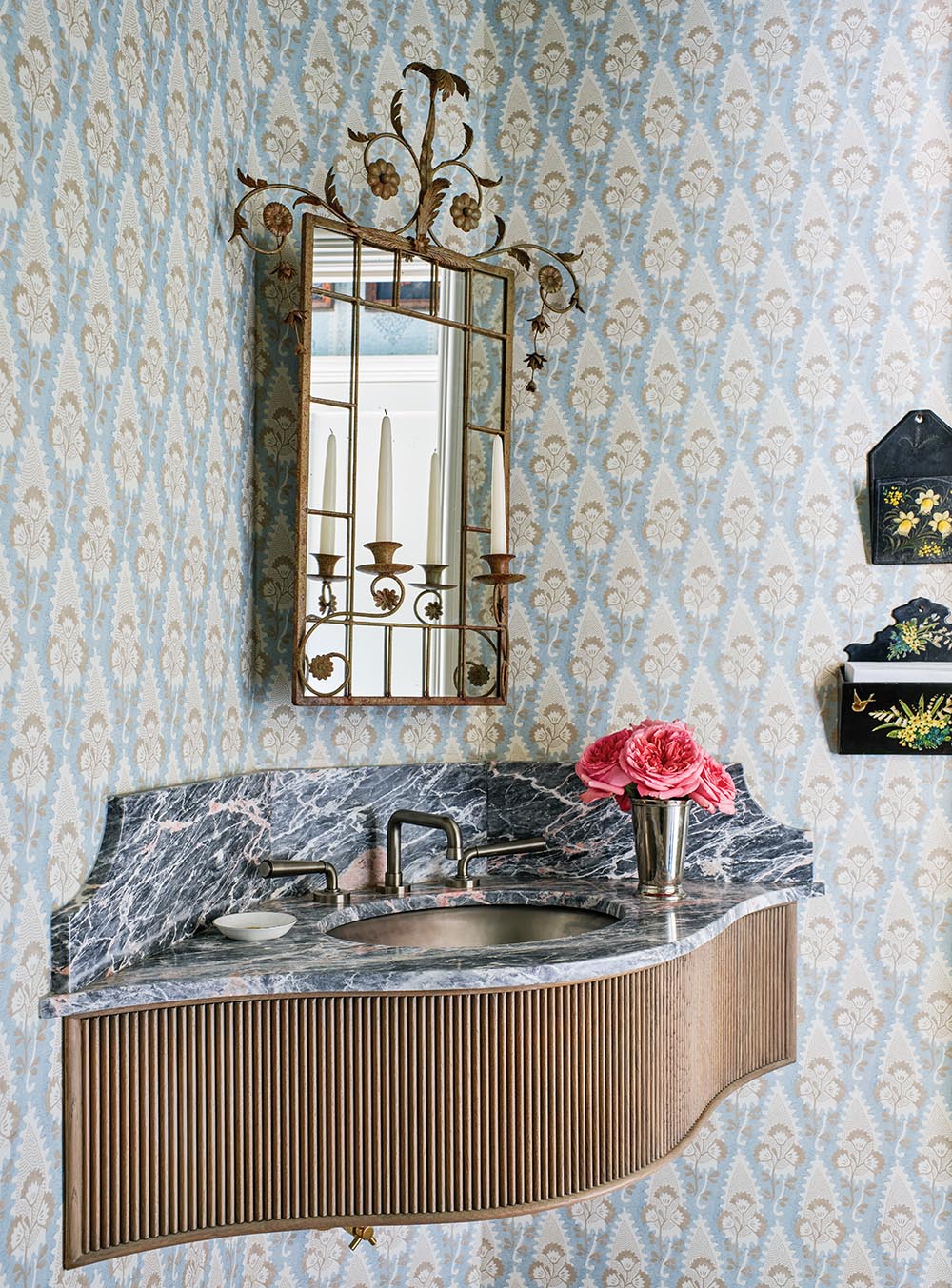 Wall-hung serpentine sink with marble top under gold, metal-framed mirror in powder room designed by Bunny Miller.