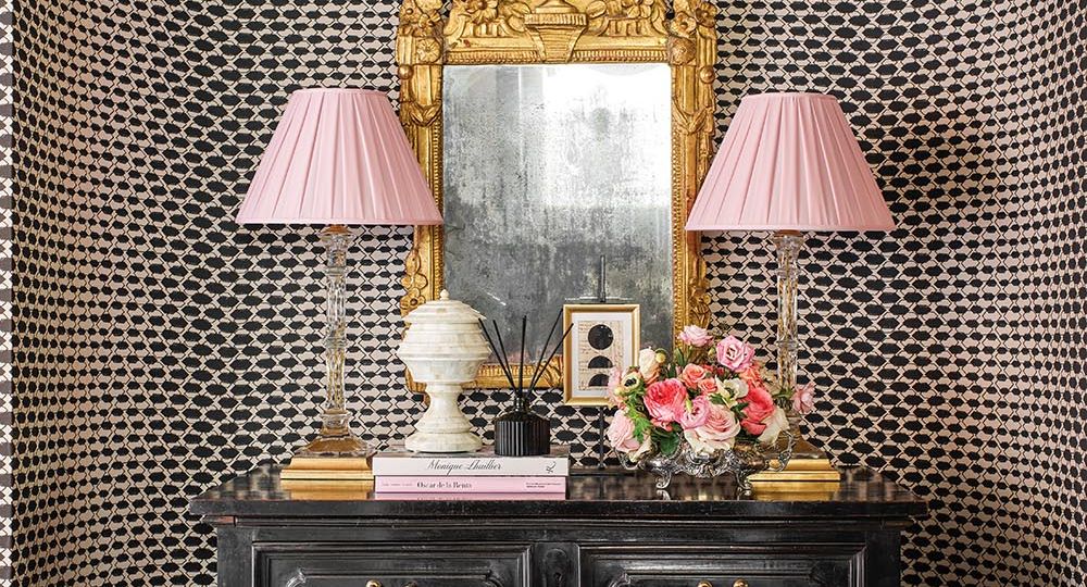 Chest in rounded nook with pair of pink-shaded lamps, arrangement of flowers by Parties to Die For and ornate gold mirror on the wall. Interior design by Julie Dodson