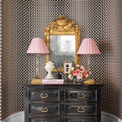 Chest in rounded nook with pair of pink-shaded lamps, arrangement of flowers by Parties to Die For and ornate gold mirror on the wall. Interior design by Julie Dodson