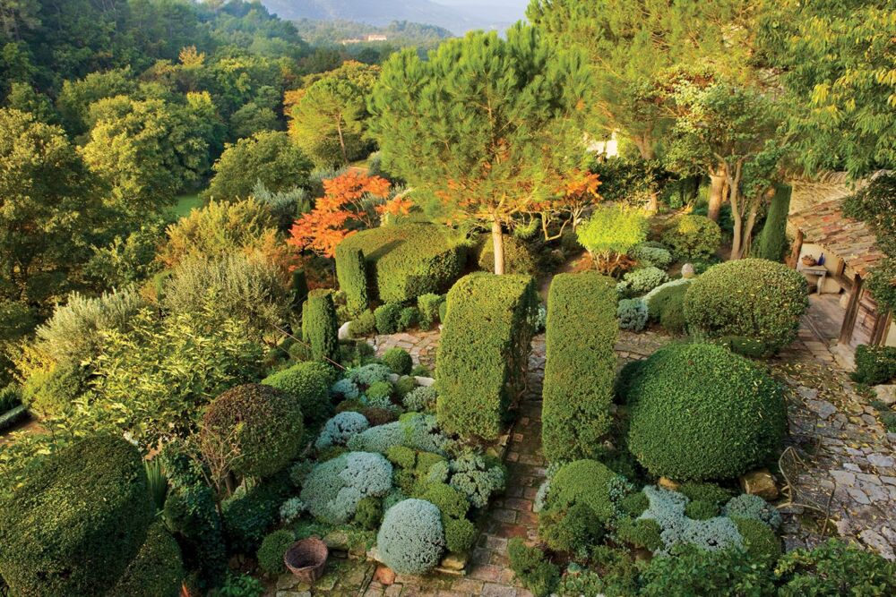 Green rounded hedges dominate a mountainous landscape.