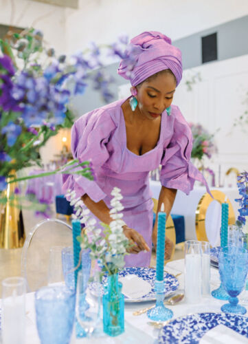 A woman dressed in purple sets a blue table.