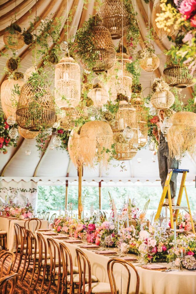 Bright seagrass lanterns hang above a table with assorted pink flowers at an event designed by Tattie Isles.
