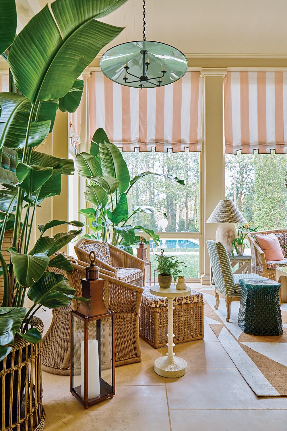 Screened porch with wicker chairs and ottoman, potted bird of paradise plants, large brass lantern on floor, pendant light with inside of shade painted haint blue.
