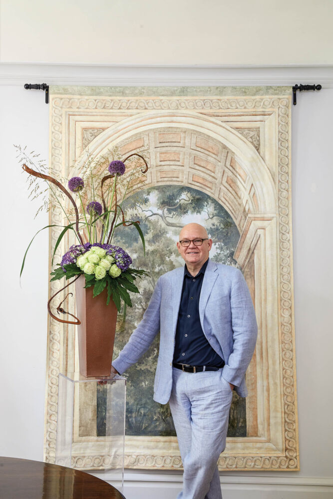 Bob Vardaman proudly stands next to his flower arrangement with inspirational Fragonard-style mural behind him.