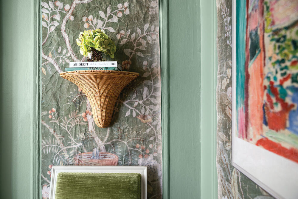 Apartment entry with chinoiserie panels from Folly Home cut to line moldings. Green hydrangeas sit on a rattan bracket centered above a chair.