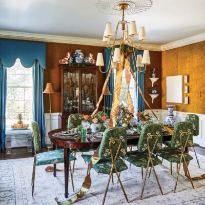 Dining room with turquoise drapery, tobacco-colored walls, green floral prints on dining chairs and gold ribbon and holiday greenery on the chandelier.