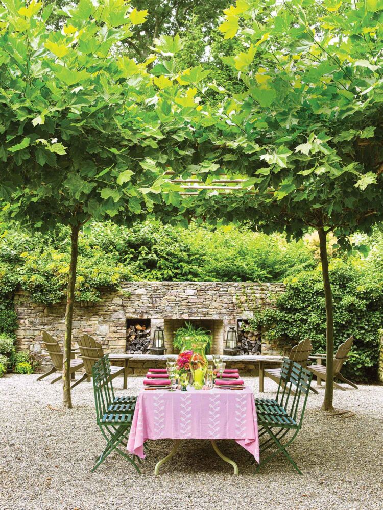 A pink tablecloth covers an outdoor table on gravel under some shady trees.