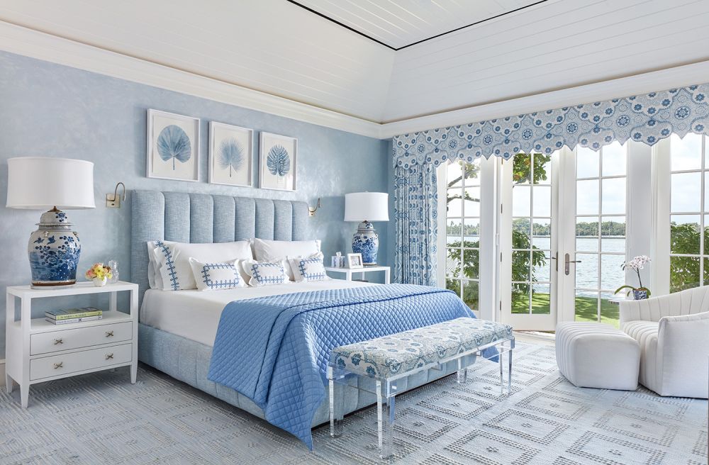 A blue quilt, wallpaper, and curtains in a bedroom.