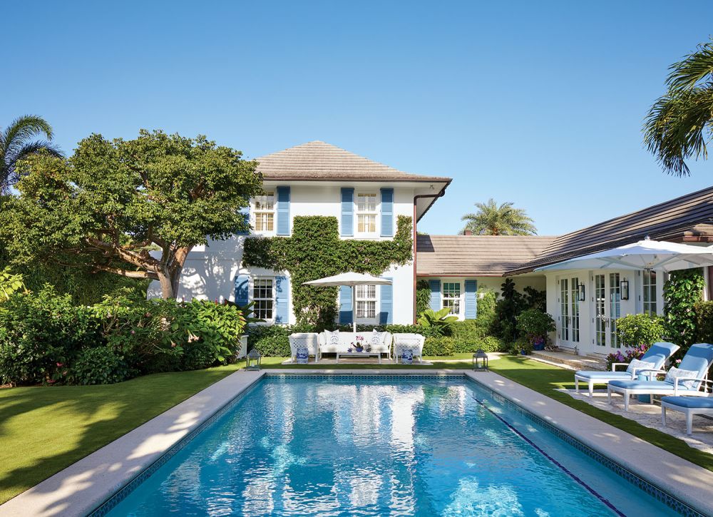 A glistening pool sits behind a house with turquoise shutters.