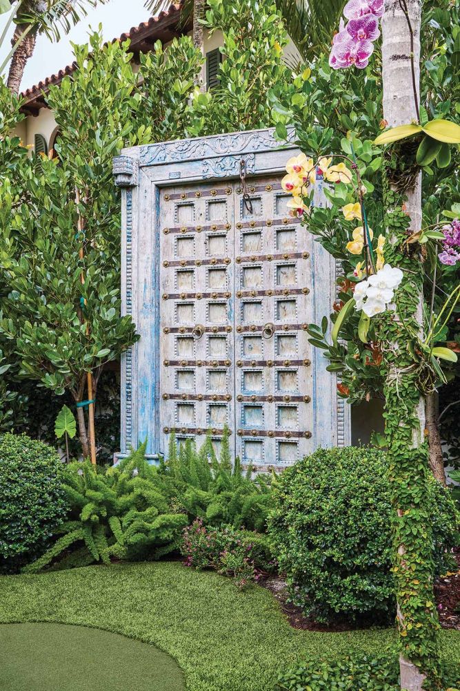 A large antique blue door sits in a garden.