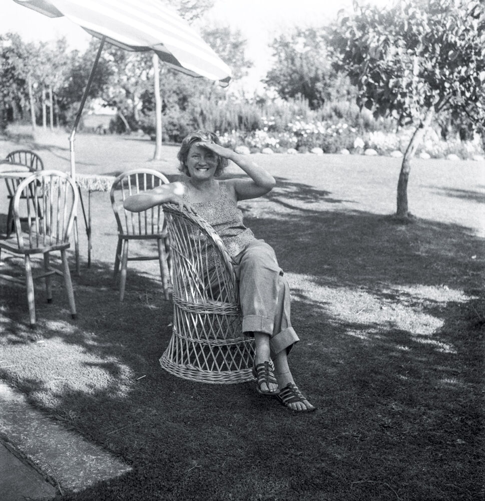 Lee Miller sitting in wicker chair in her garden.