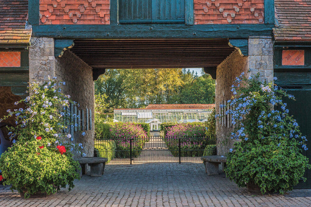 Entrance to the walled garden at Eythrope, flanked by pots of blue Plumbago and scarlet Palangonium