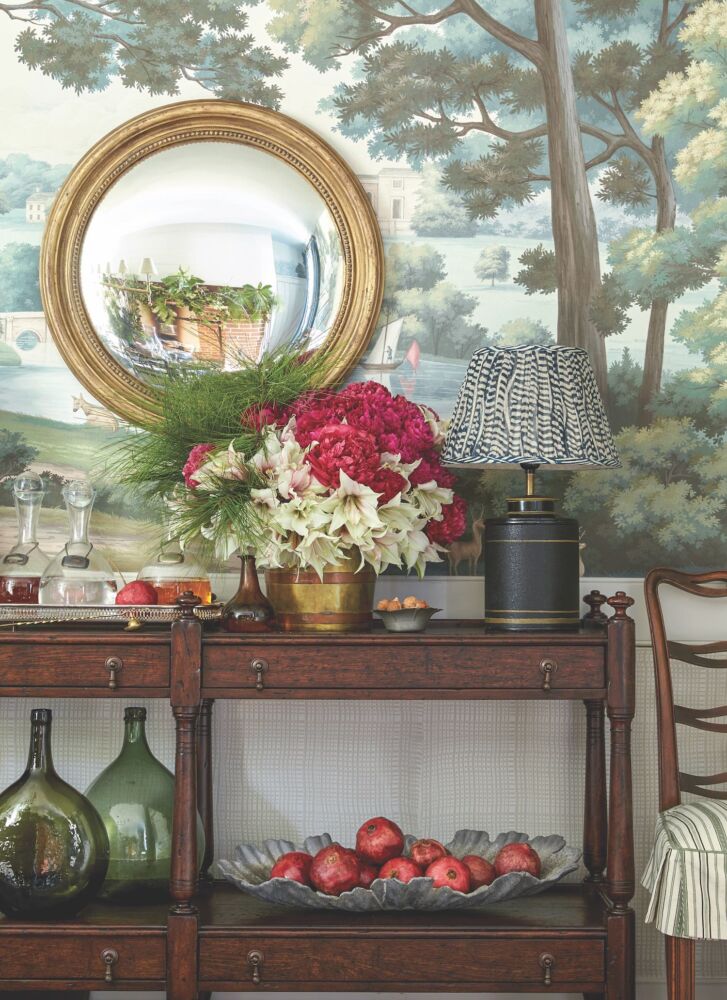 An arrangement of peonies, amaryllis, and pine sits before a backdrop of a Regency Views mural inside the Williamsburg home designed by Heather Chadduck.