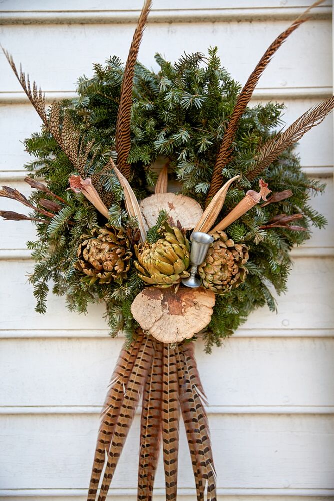 Bird feathers and dried artichokes are pinned to an evergreen wreath.