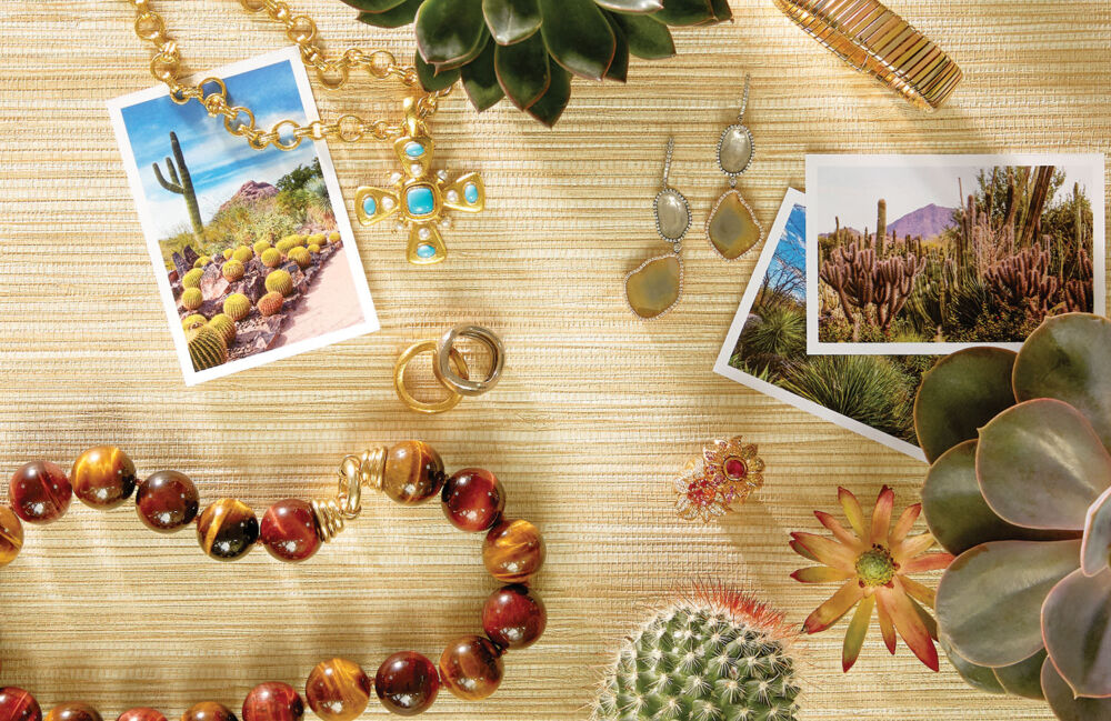 A beaded necklace, a turquoise necklace, a pair of drop earrings, and ruby rings lay next to pictures of the American Southwest desert.