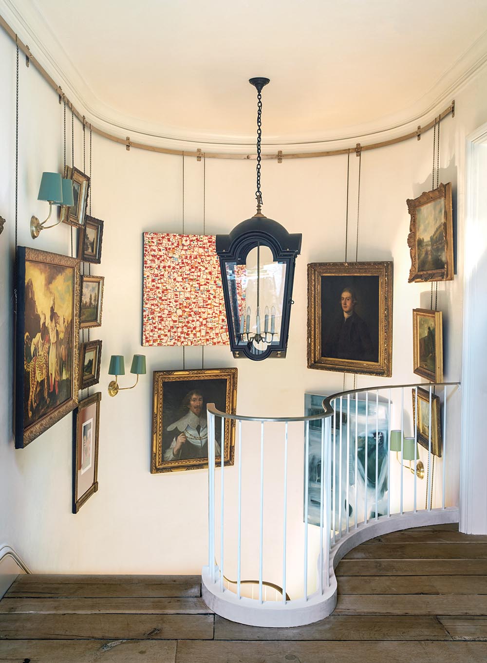 Large lantern hanging above stairs at second-story landing. Brass rail system holds paintings hung in stairwell.