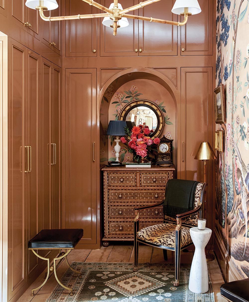Arched niche with chest that is topped with lamp, arrangement of dahlias and mums, and chinoiserie clock in gentleman's dressing room designed by Nina Long and Don Easterling.