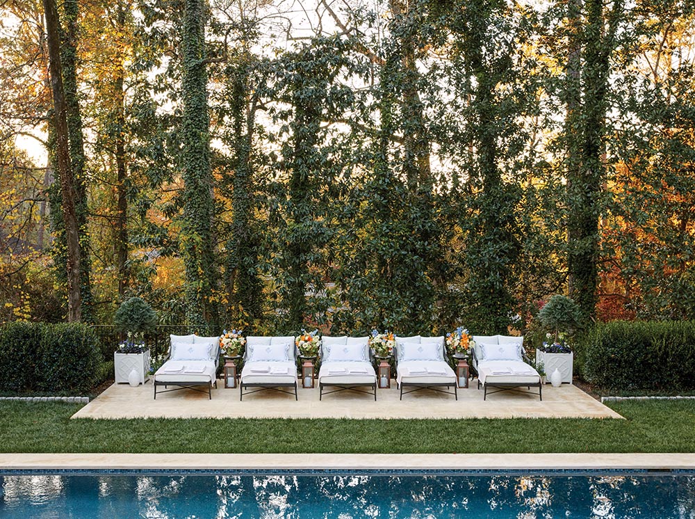 Poolside line of five oversized lounge chairs with brass lanterns and small tables topped with flower arrangements by Canaan Marshall between the chairs.