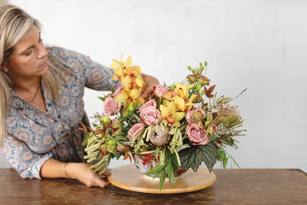 Holly Bryan adding Rex begonia and yellow Cymbidium orchids to flower arrangement.