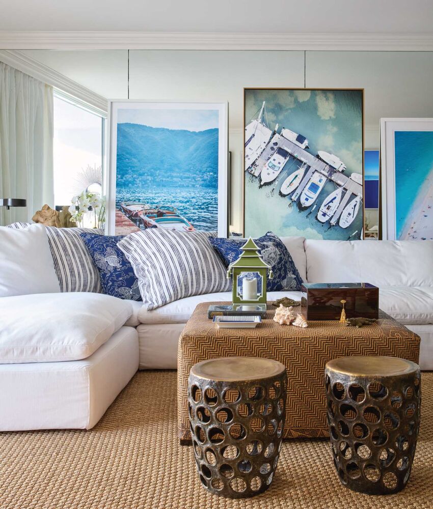 White sectional sofa with blue and white throw pillows and bronze stools. Boat and beach photos on the wall.