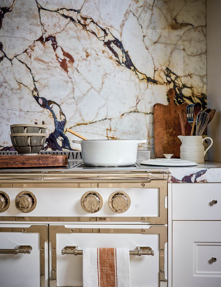 A white and gold stove with a marble backsplash.