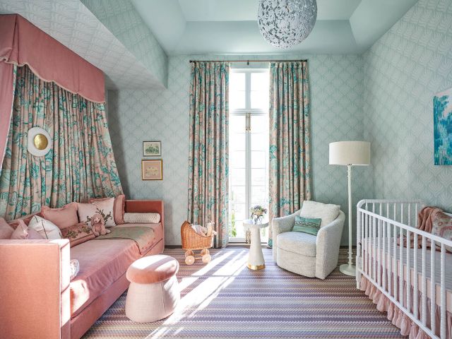 Light shines through a window into a light turquoise nursery with a pink bed.