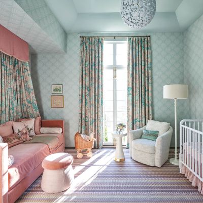 Light shines through a window into a light turquoise nursery with a pink bed.