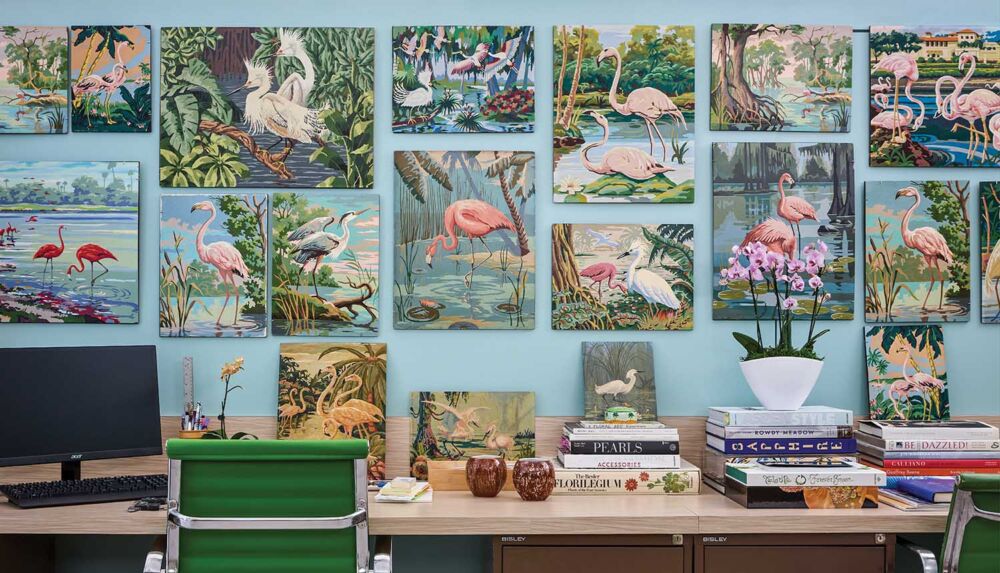 Office with walls covered in kitschy ‘50s and ‘60s “paint by numbers” flamingo paintings.