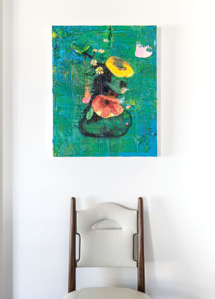 An abstract art piece with a green background and yellow and pink flowers hangs above a plain grey chair.